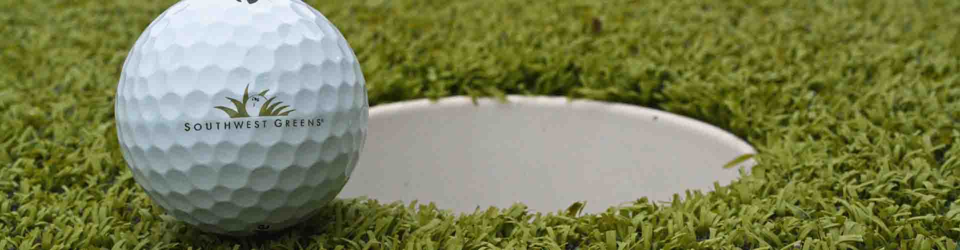 Close-up of a golf ball resting on artificial turf beside the cup on a professionally installed backyard putting green designed for realistic at-home golf practice.