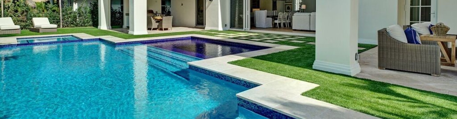 Southwest Greens lawn turf grass bordering a luxury residential pool and spa with travertine pavers and outdoor living space.