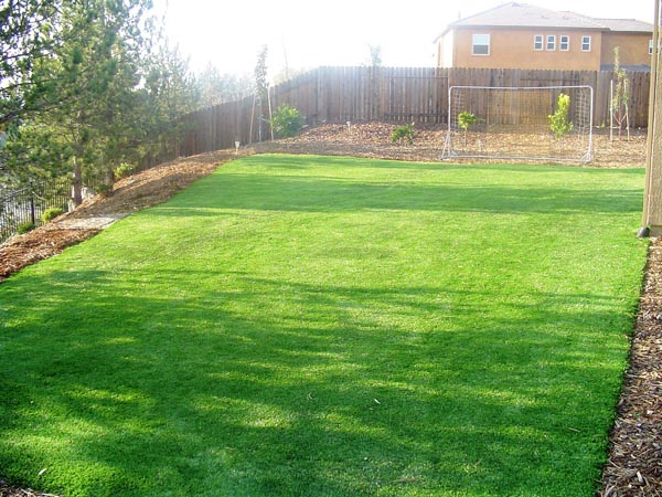 Fake grass installation in fenced residential backyard with soccer goal and wood privacy fence