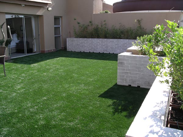 Fake grass installation in enclosed Southwest patio with white brick raised planters and sliding glass door access