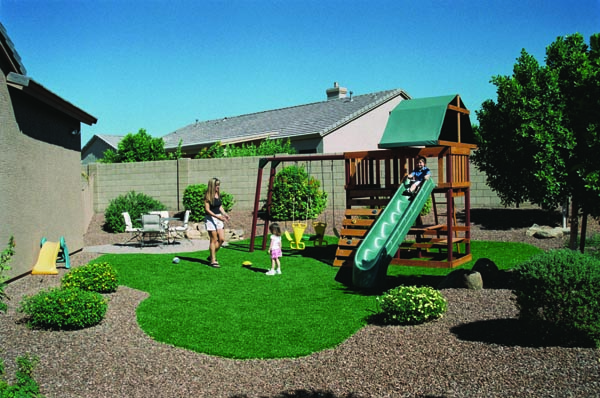 Family enjoying artificial grass backyard with wooden swing set, putting green, and desert gravel landscaping