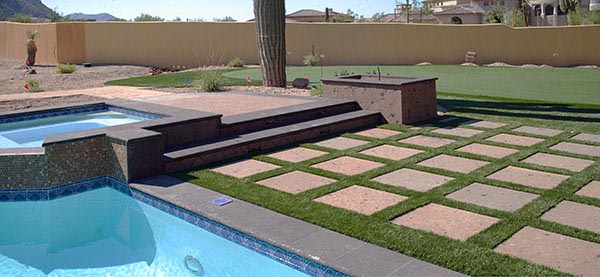 Synthetic grass installation with square stepping stone grid alongside residential pool and spa in Southwest desert backyard