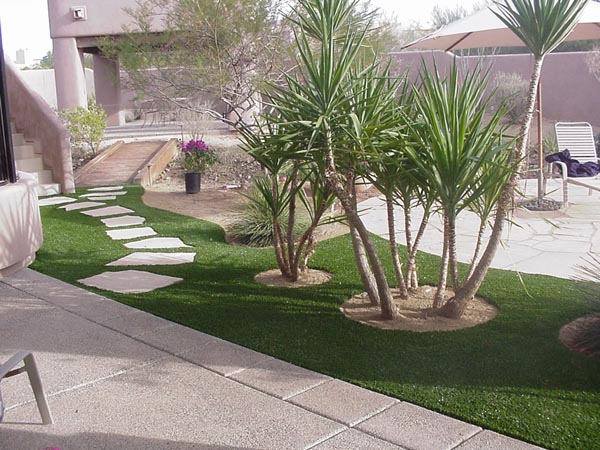 Synthetic grass installation with natural stone stepping path and yucca trees in Southwest residential front yard landscape