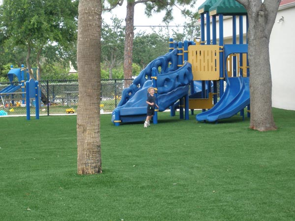 Child playing on artificial grass surface beneath blue and yellow multi-slide commercial playground structure with palm trees