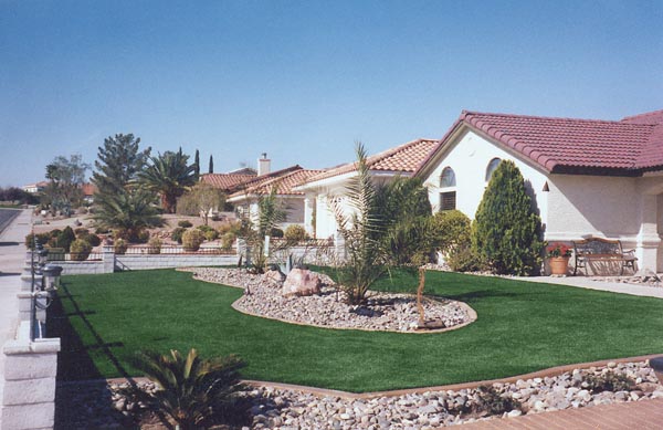 Artificial grass front yard with decorative rock borders and desert plantings at Southwest Mediterranean-style home