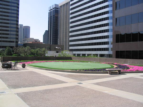 Best artificial lawn oval green space with pink flower border installed at downtown commercial plaza surrounded by high-rise office buildings
