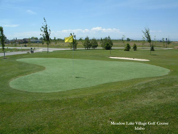 Artificial turf golf course putting green with yellow flag and sand bunker at Meadow Lake Village Golf Course in Idaho