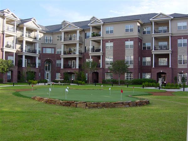 Artificial golf green with multiple flags and stone retaining wall surround at upscale brick apartment complex courtyard