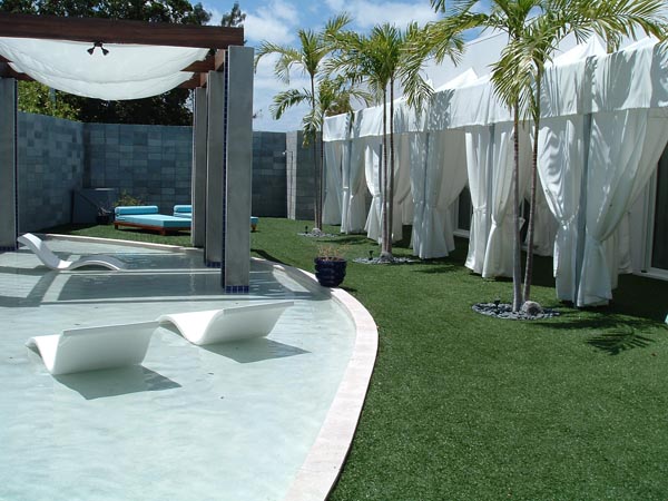 Artificial turf installation alongside luxury pool and cabana area with palm trees at upscale resort or hotel property