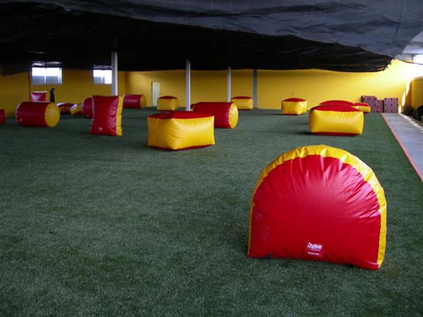 Indoor artificial turf installation at paintball arena with red and yellow inflatable obstacles inside warehouse facility