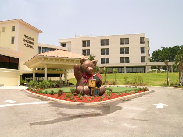 Artificial turf installation at Nicklaus Children's Hospital entrance with decorative bear statue and tropical landscaping