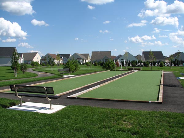 Artificial grass bocce ball courts at residential community with benches, green lawns, and neighborhood homes in background