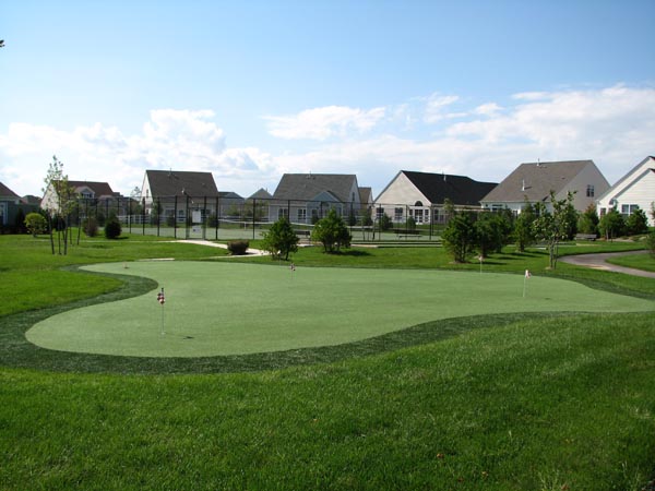 Artificial grass putting green with multiple flags and sand bunker at upscale residential community recreation area