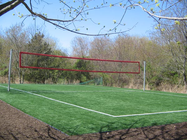 Outdoor artificial grass volleyball court with red net and white boundary lines surrounded by natural wooded landscape