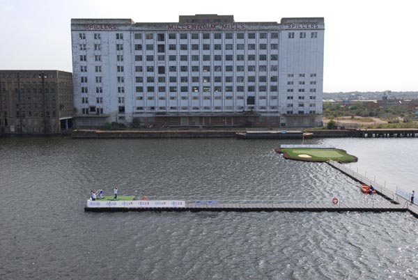 Floating artificial grass putting green and tee box platform on urban waterway during outdoor golf event