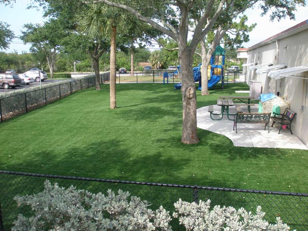 Artificial turf lawn with mature trees and outdoor seating area at commercial property next to children's playground
