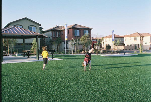 Children playing and doing cartwheels on artificial turf community green space in residential neighborhood