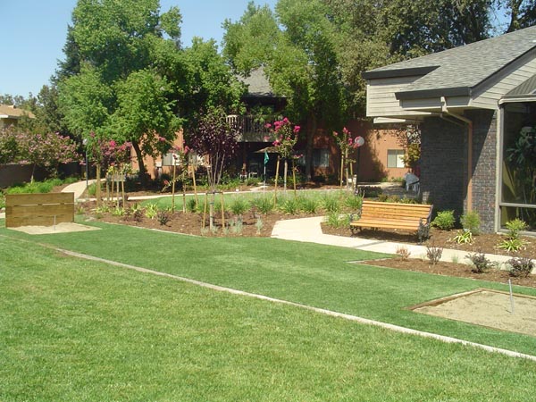 Artificial turf horseshow pit with wooden borders and garden bench installed in residential backyard landscape