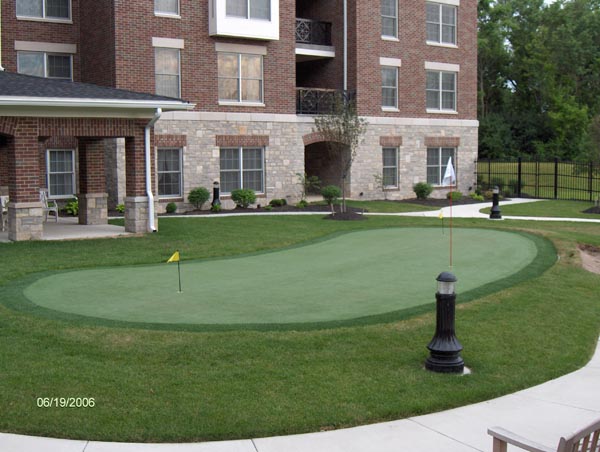 Synthetic turf putting green with two yellow flags installed in courtyard of upscale brick apartment complex
