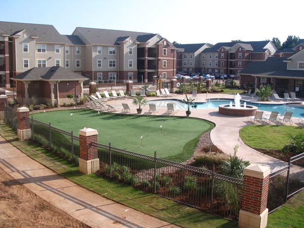 Synthetic turf putting green with iron fence surround at luxury apartment complex pool and recreation area
