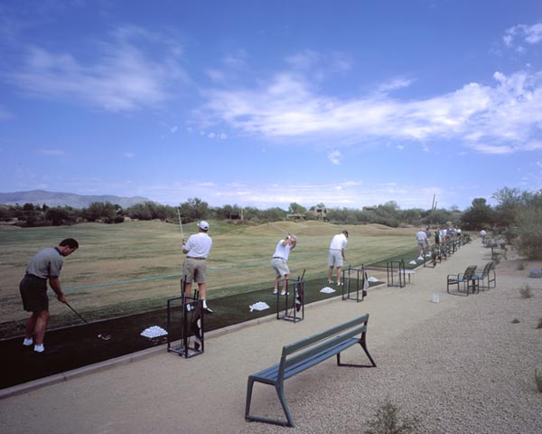 Golfers hitting from artificial turf tee lines at Southwest desert golf driving range with mountain backdrop