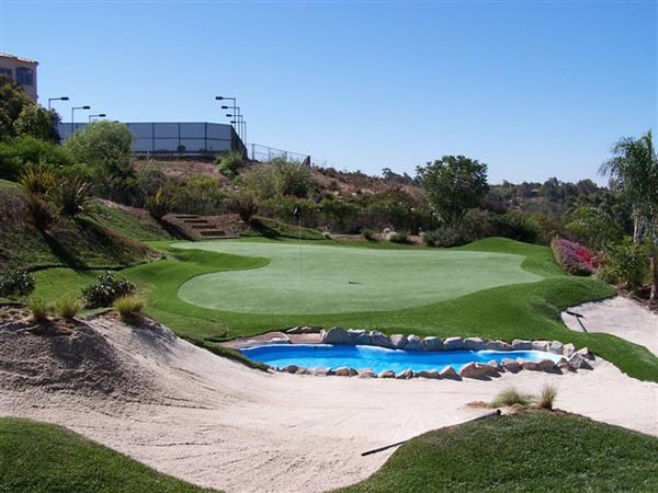 Backyard putting green with decorative pond water feature, sand bunkers, and hillside desert landscaping