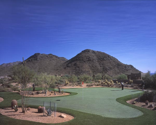 Golfer putting on backyard putting green with dramatic Southwest desert mountain backdrop and saguaro cactus landscape