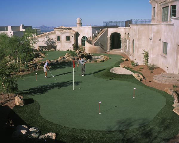 Two golfers playing on backyard putting greens with boulder landscaping at Southwest luxury estate with mountain views