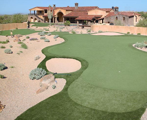 Large backyard putting greens with sand bunker and desert rock landscaping at Southwest hacienda-style luxury estate