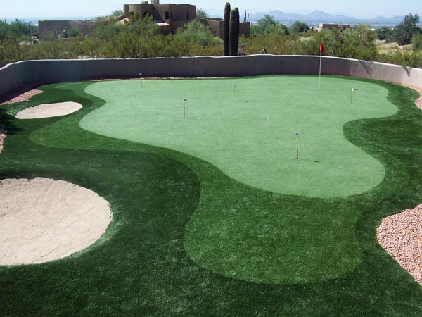 Backyard putting green with multiple holes, sand bunkers, and desert rock landscaping surrounded by stucco wall in Southwest home