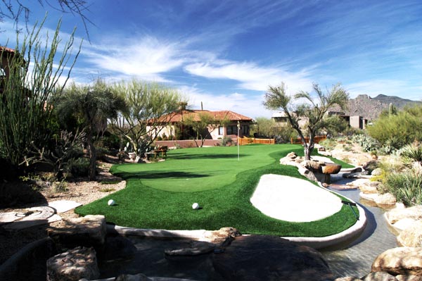 Putting green turf with sand bunker and boulder rock landscaping at Southwest desert luxury home with mountain backdrop
