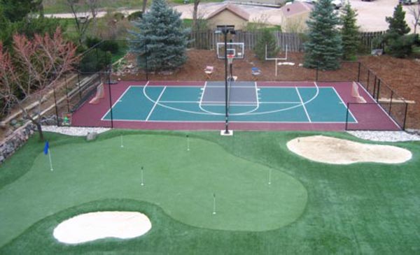 Backyard putting greens with sand bunkers and blue flag alongside full basketball court in residential sports yard