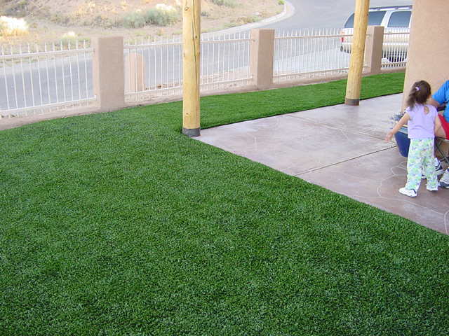 Fake grass installation at Southwest home entrance with concrete patio and wood post columns next to children playing