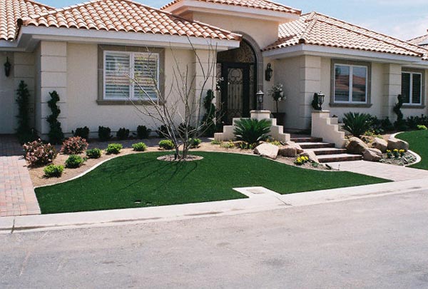Fake grass installation in front yard of Southwest Mediterranean-style home with desert rock and shrub landscaping