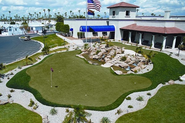 A commercial putting green surrounded by buildings and a parking lot